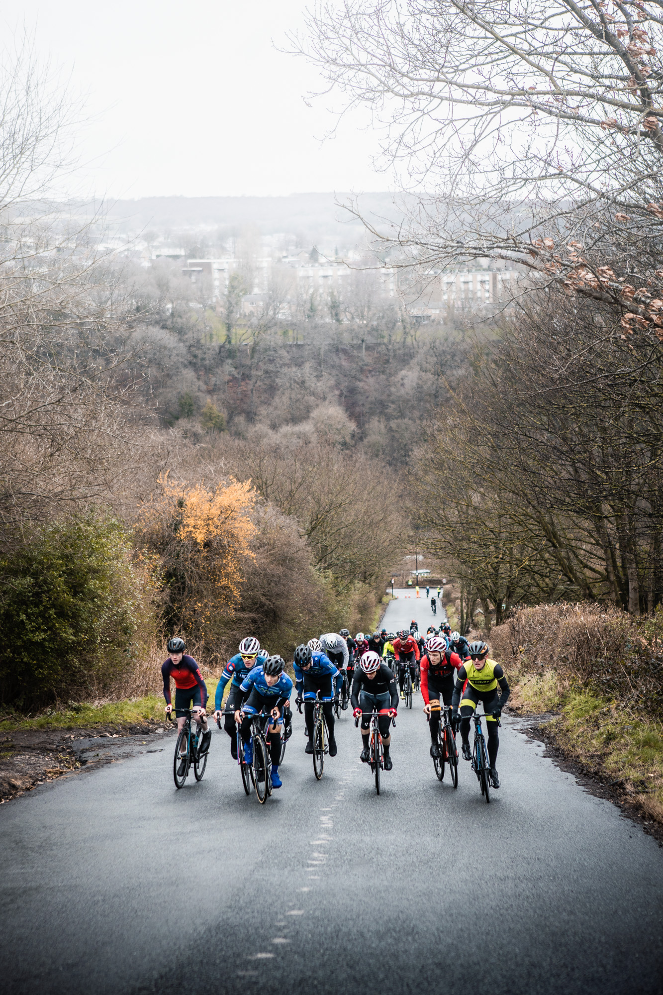 A group of cyclists riding uphill on the road, with part of the city in shot in the distance.