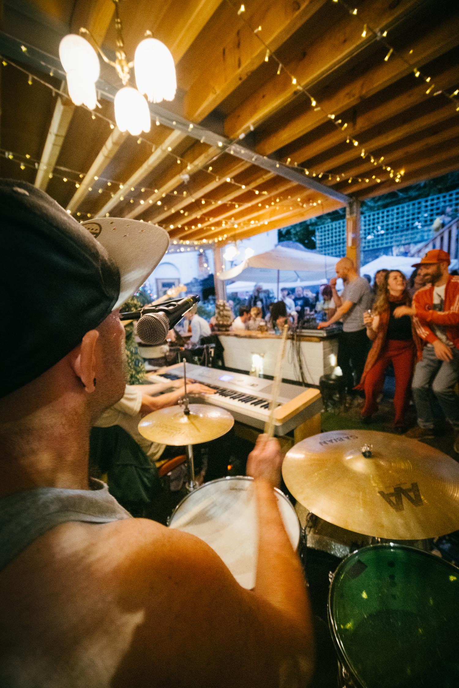 People gathered round, at dusk, listening to a band play in an outdoor setting.