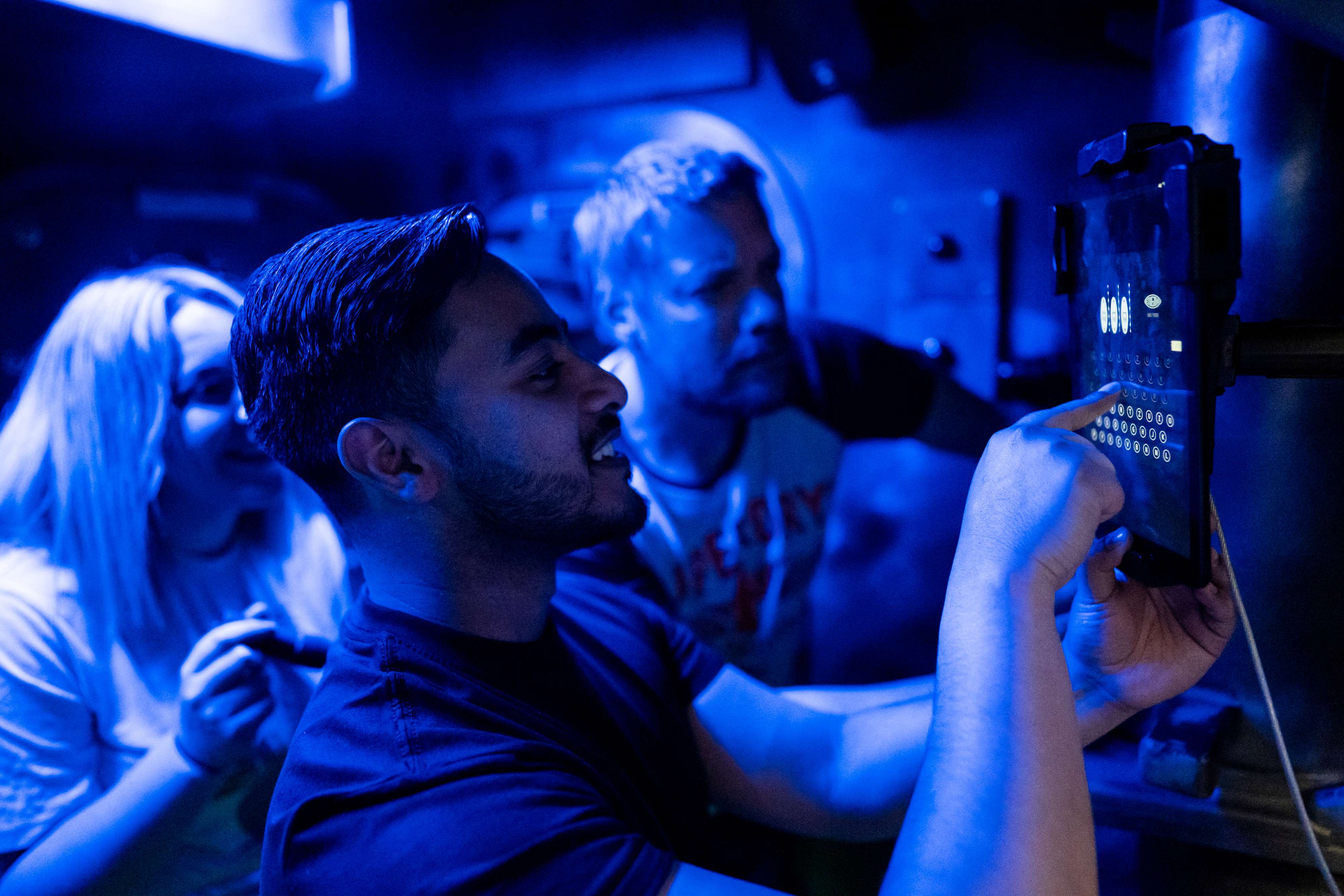 Three people in a room dimly lit by blue light are solving a puzzle at The Great Escape.