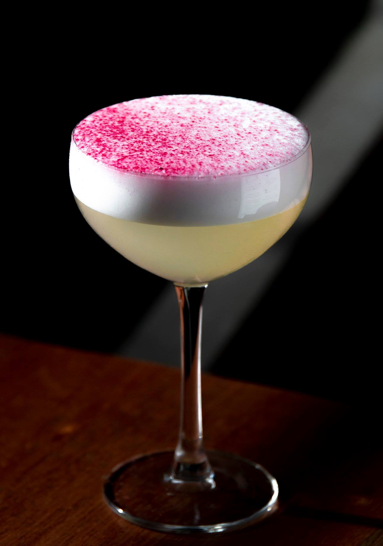 A yellow cocktails with a pink dusting on top.