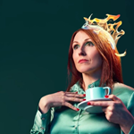 A woman, looking distracted, in a green dress holding a cup of tea. There are flames on her hair.