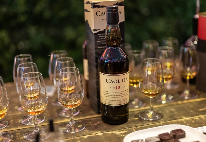 A bottle of single malt whisky is stood on a table surrounded by tasting glasses filled with a sample of the Whisky.