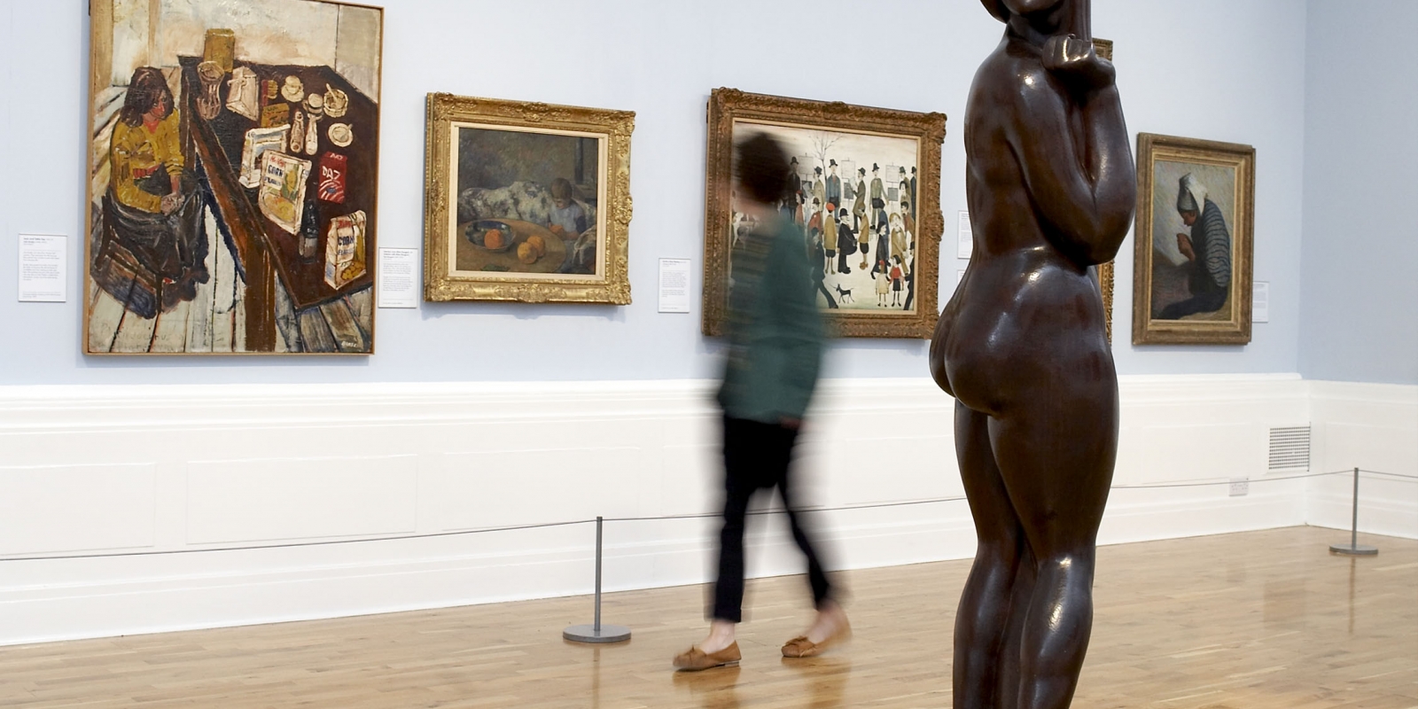 Inside Graves Gallery a woman is standing in front of three paintings.