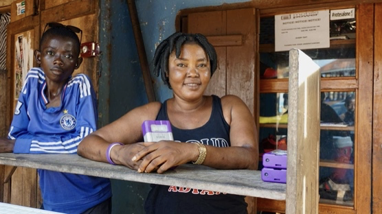 Two women stand leaning on a wooden shelf, looking directly at the camera and smiling.