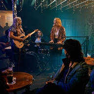 A three piece band plays live in front of a crowd at Alder.