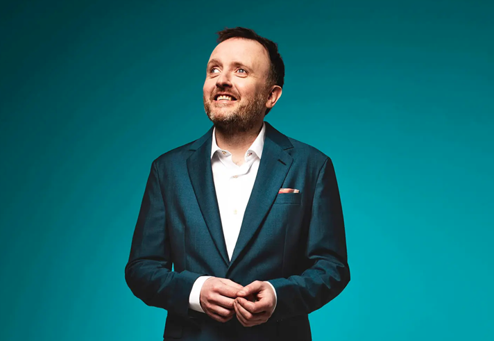 A portrait of Chris Mccausland, in a smart green suit, smiling.