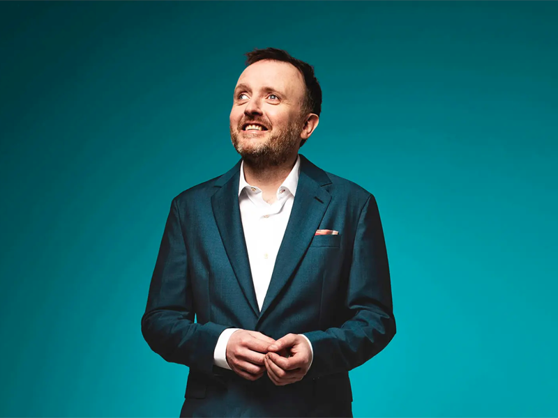 A portrait of Chris Mccausland, in a smart green suit, smiling.