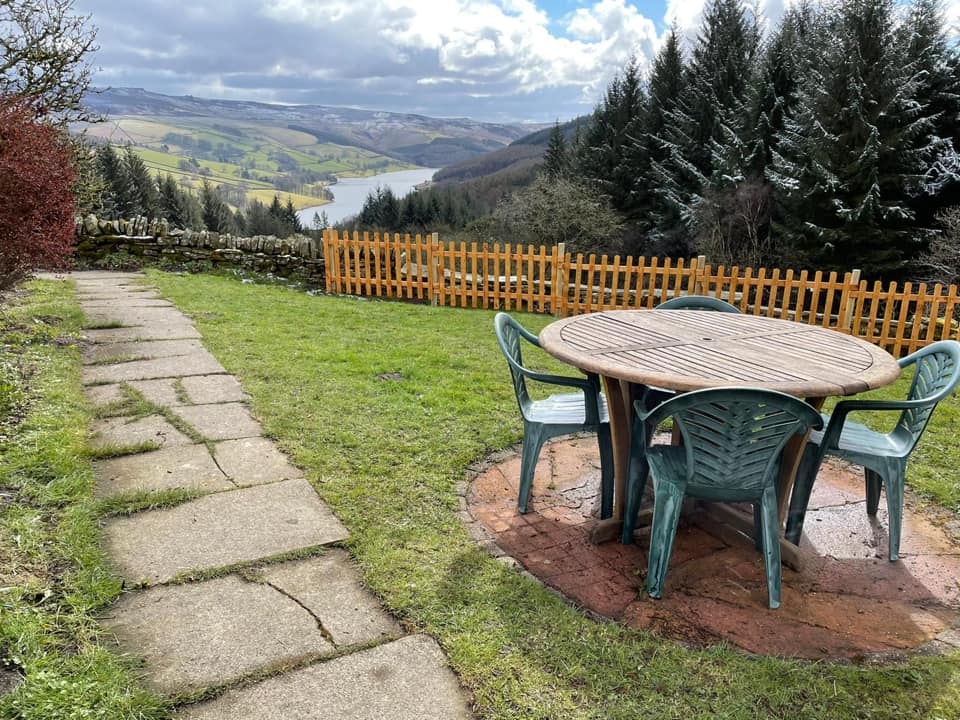 A table and chairs in a garden, overlooking a valley.