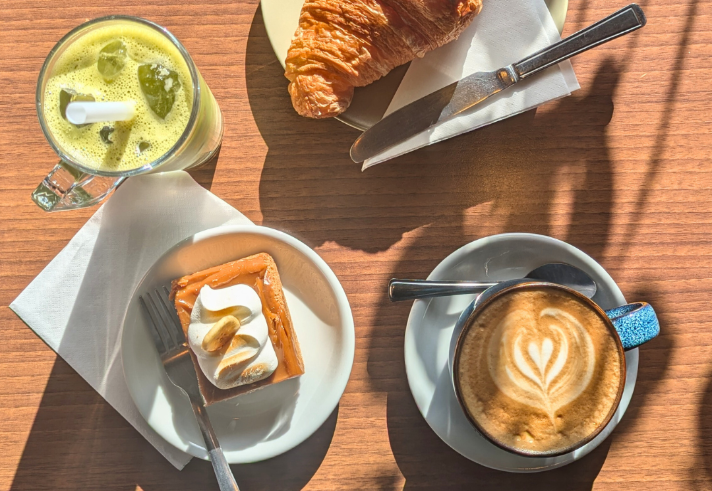 A wooden table, in the sun, with a coffee, delicious pastries and a smoothie at the Copper Pot Café.