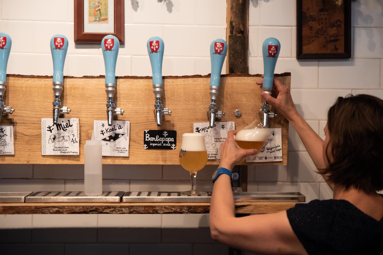 A woman, with her back to the camera, is pulling a glass of beer from a traditional beer pump.