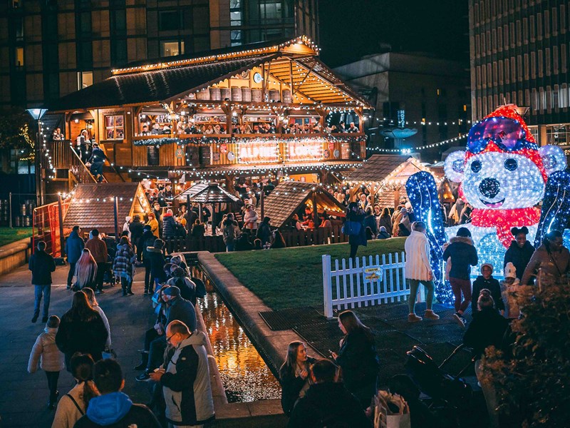 An Alpine Lodge, lit up with fairy lights, sits in the middle of the Peace Gardens as part of the Sheffield Christmas Market. In the foreground is a huge light-up polar bear.