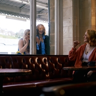 Two women stand outside a window at The Sheffield Tap, while a third (sat inside) gestures for them to come in.