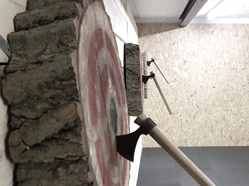 Three wooden targets on a wall, each with a throwing axe in the bullseye.