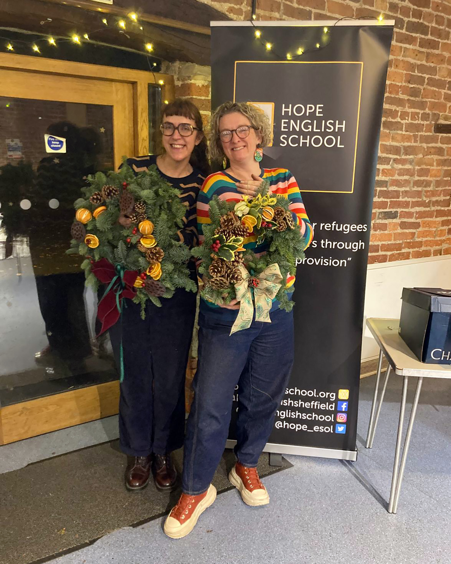 Two women proudly holding Christmas wreaths that they have made.