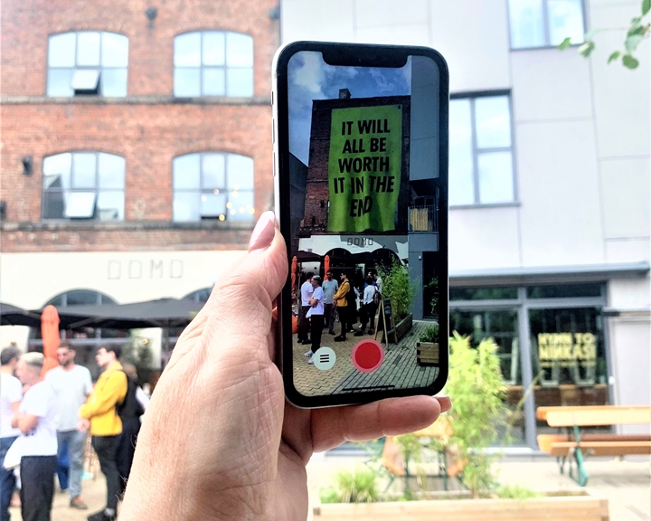 A hand holds up a mobile phone showing the Corbin Shaw artwork that is part of the Look Up! AR art trail in Sheffield.