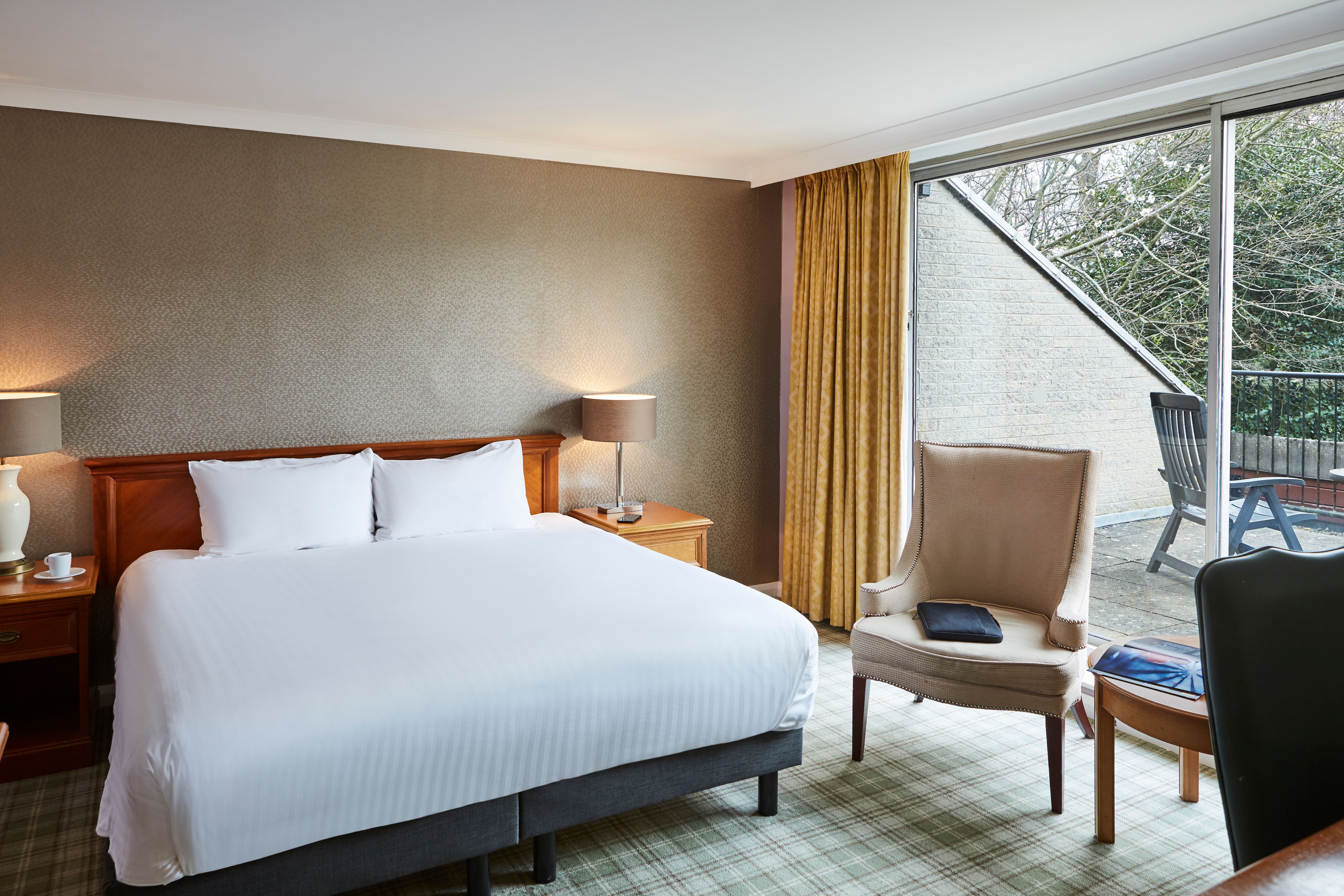 Bedroom with crisp white bedding and a armchair positioned in front of a large window allowing ample natural light.