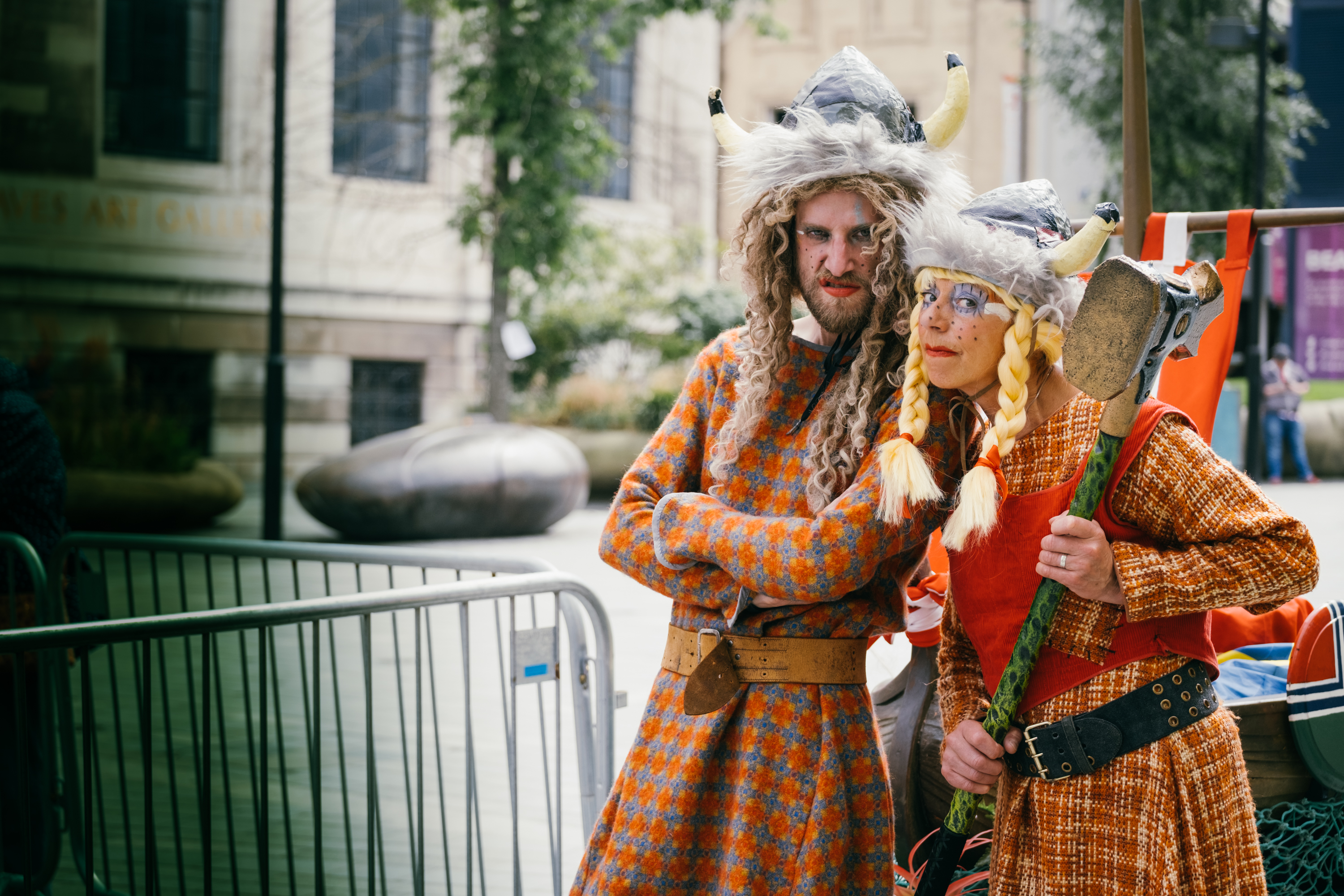 A man and a woman stand in Tudor Square, pulling faces at the camera, dressed as Vikings but with a humorous twist.