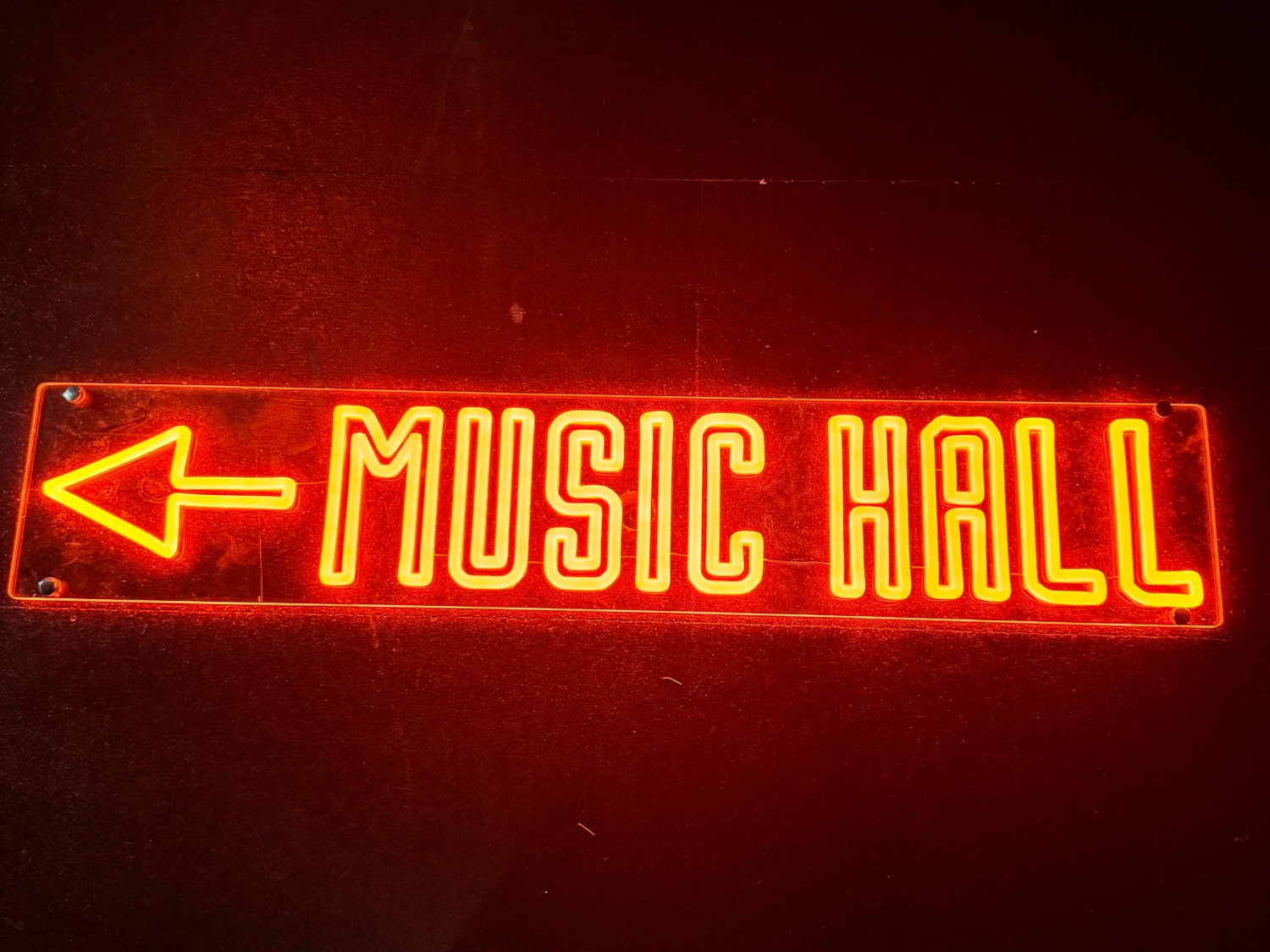 A red neon sign that reads 'Music Hall' with an arrow pointing left.