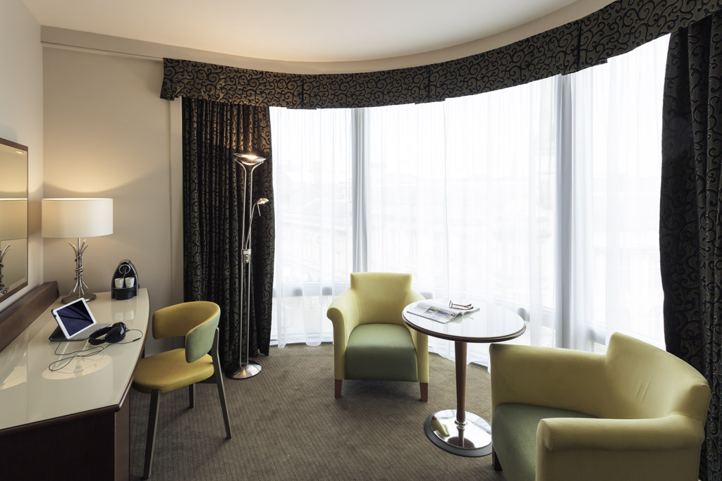 Spacious sitting area in a junior suite featuring a coffee table, armchair, and large windows with natural light