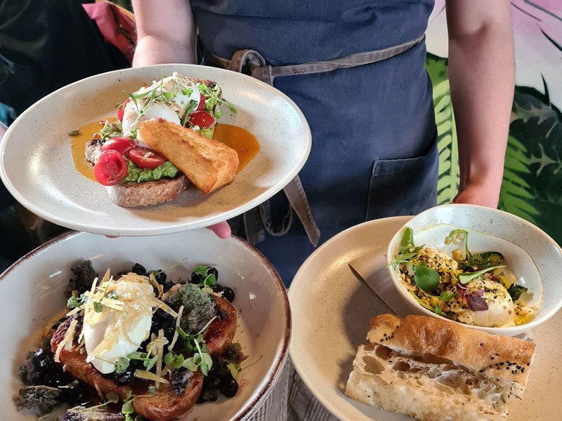 A member of Tamper Coffee staff carrying three plates of food to a table.