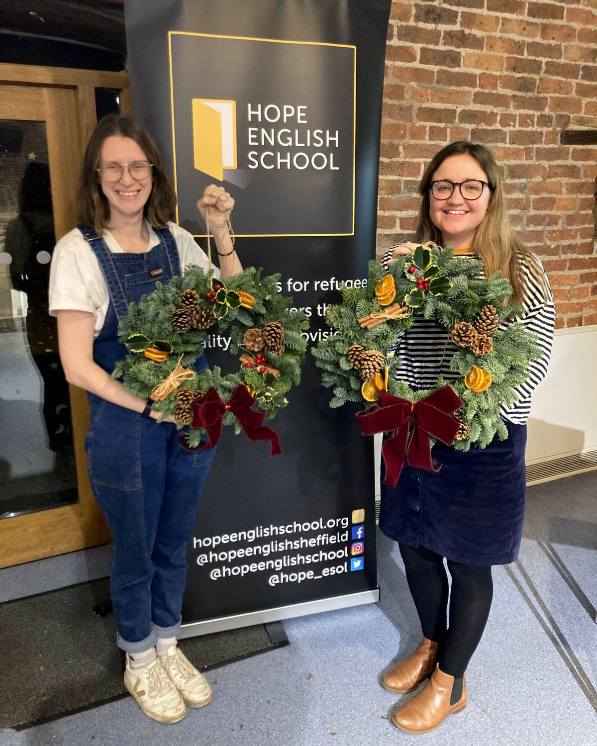 Two women proudly holding Christmas wreaths that they have made.