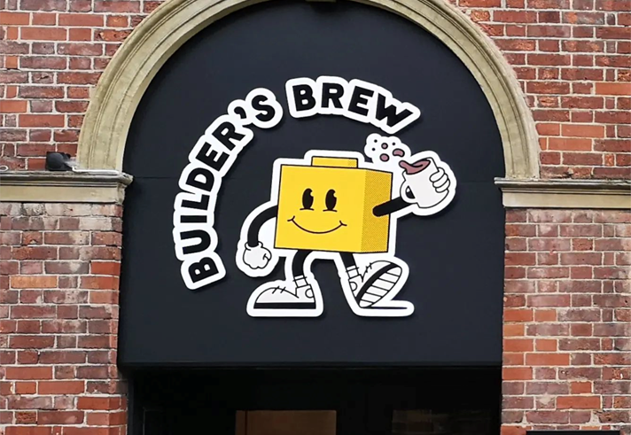Builder's Brew Café logo on the outside of a building. The logo has the words 'Builder's Brew' round a cartoon character, who is shaped like a toy building brick, holding a mug of tea.