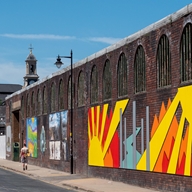 A large brick wall, in Kelham Island, decorated with bright and cheerful street art.