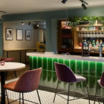 Hotel bar area with a green front, surrounded by tables and chairs for guests.
