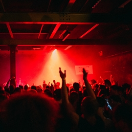 A night club lit by red light is packed with people dancing to music.