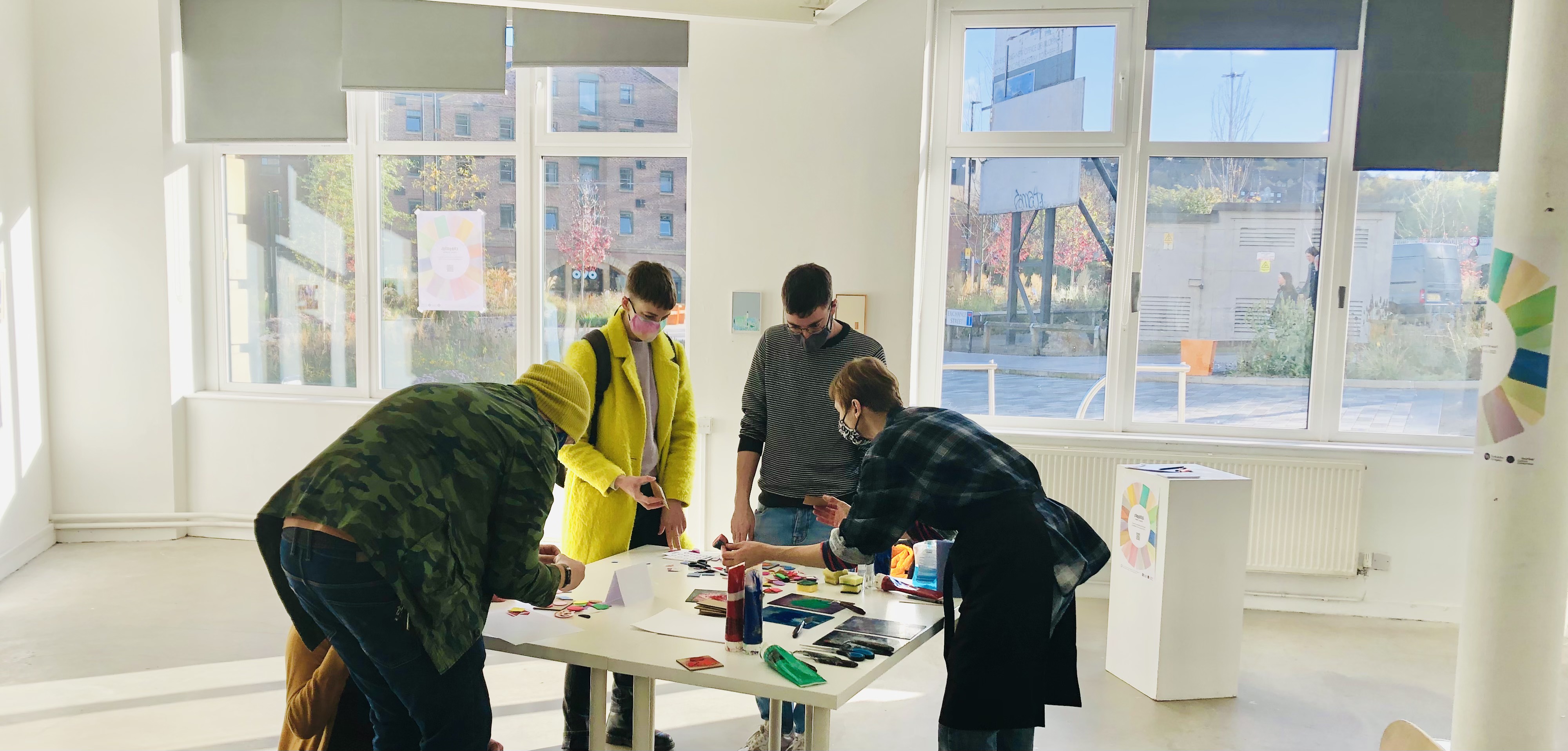 Four people stood round a table, taking part in a print making workshop.