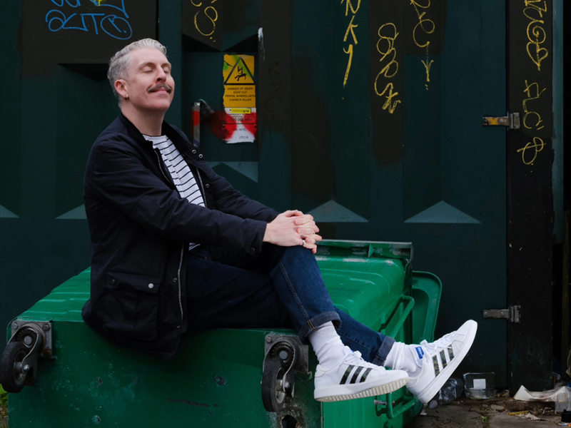 A photo of Carl Donnelly, sitting on a huge industrial rubbish bin.