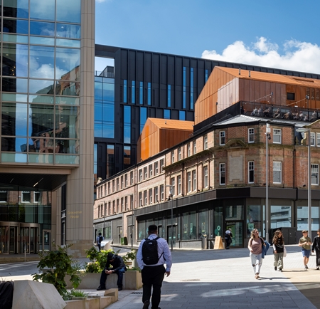 People walking in the sunshine in a pedestrian area that leads up to the food hall Cambridge Street Collective.