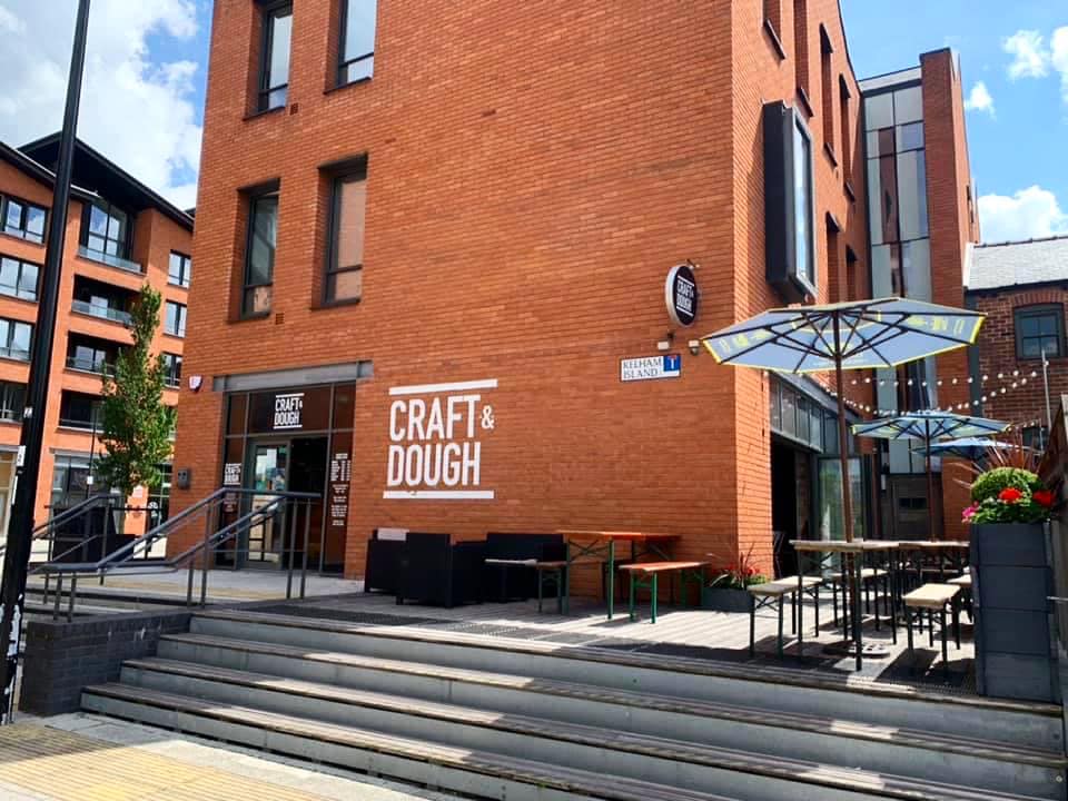 The exterior of Craft And Dough, a red brick building, with their logo painted on the wall.