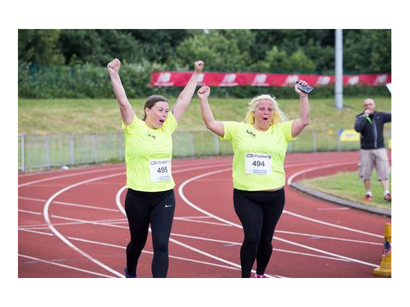 People on a race track, wearing running clothing, with their arms in the air.