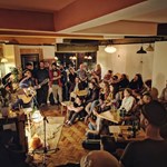 A man plays an acoustic guitar and sings in front of a small crowd at Kopi & Chai.