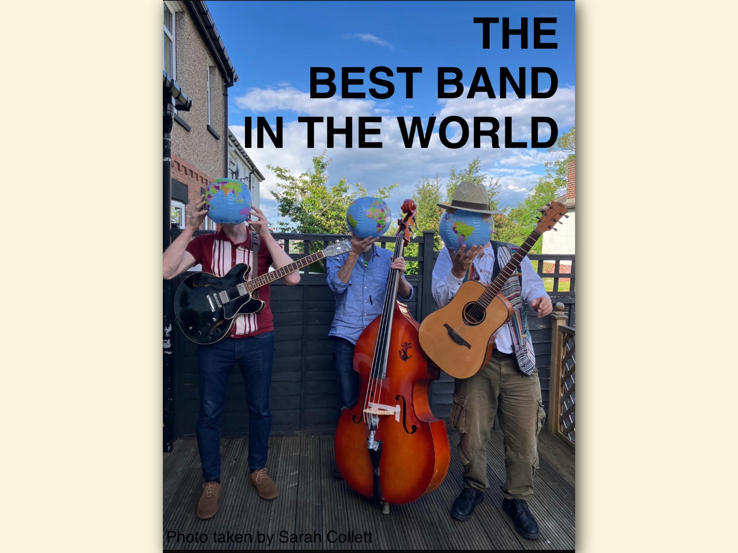 Three musicians standing on a wooden deck outdoors, each holding an instrument: an electric guitar, an upright bass, and an acoustic guitar. They are positioned in front of a black fence with houses and trees in the background under a partly cloudy sky. Large text above them reads “THE BEST BAND IN THE WORLD,” and a photo credit at the bottom says “Photo taken by Sarah Collett.” Each musician has a small globe placed over the head area as part of the design.