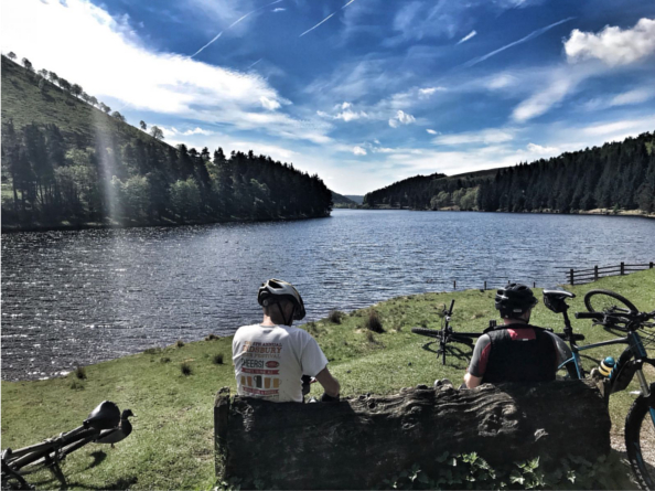 Two people sat by a lake, having a break while road cycling.