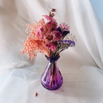 A small purple glass vase with a bunch of flowers.