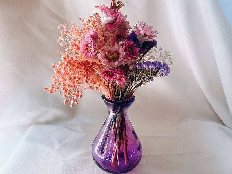 A small purple glass vase with a bunch of flowers.