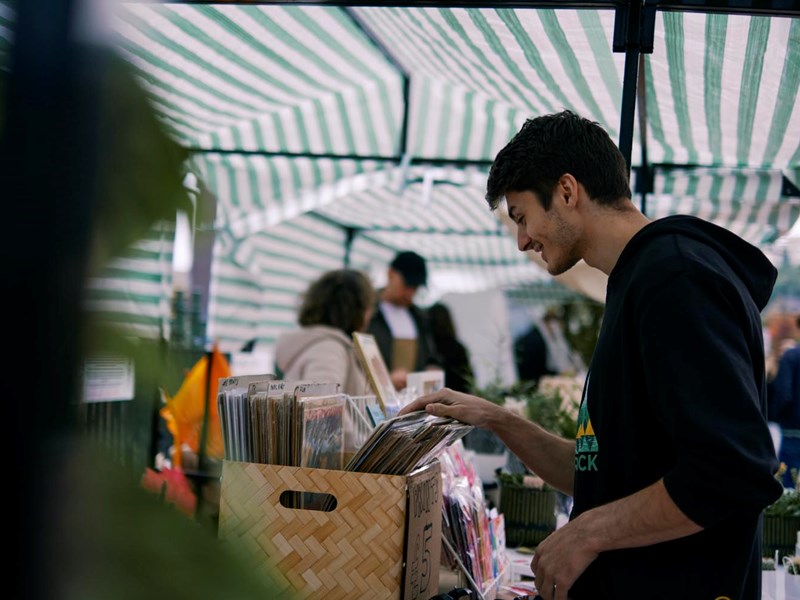 A man wearing a hoodie browsing through a box of vinyls