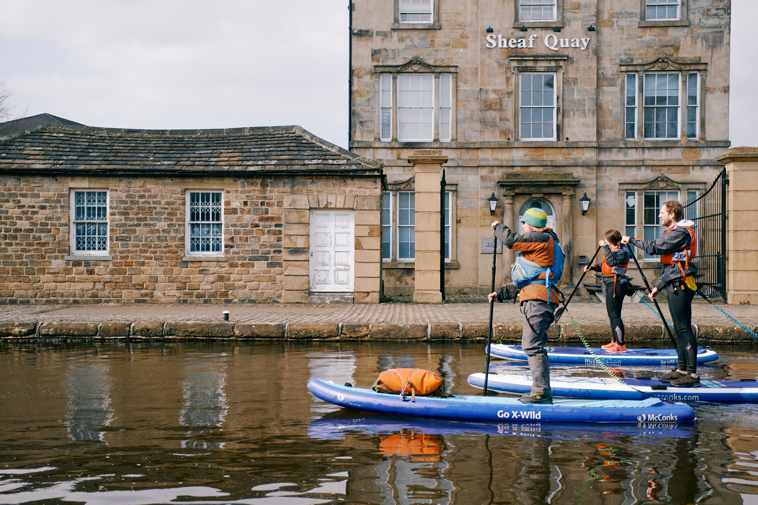Dan Crawford Outdoors leading a Stand Up Paddleboarding session along Victoria Quays - two participants are following behind as they pass the Sheaf Quay building.