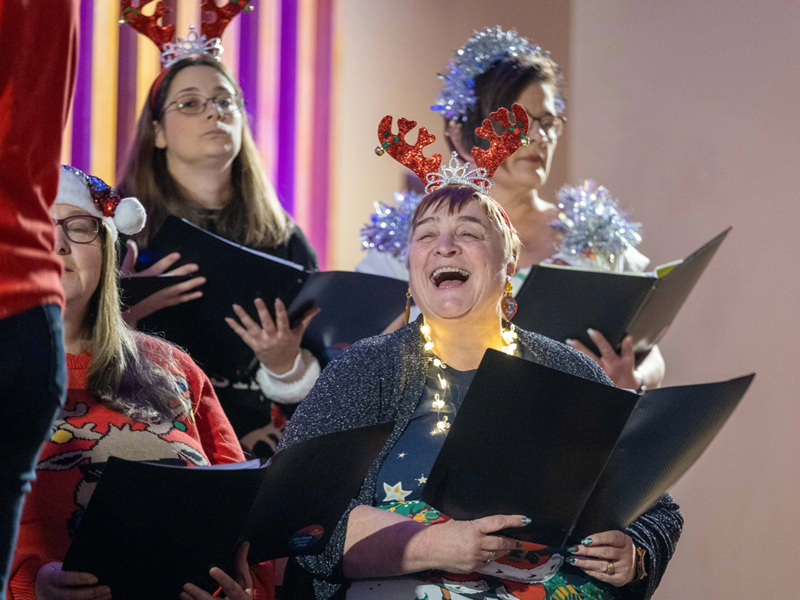 A choir, dressed in festive Christmas themed attire, performing.