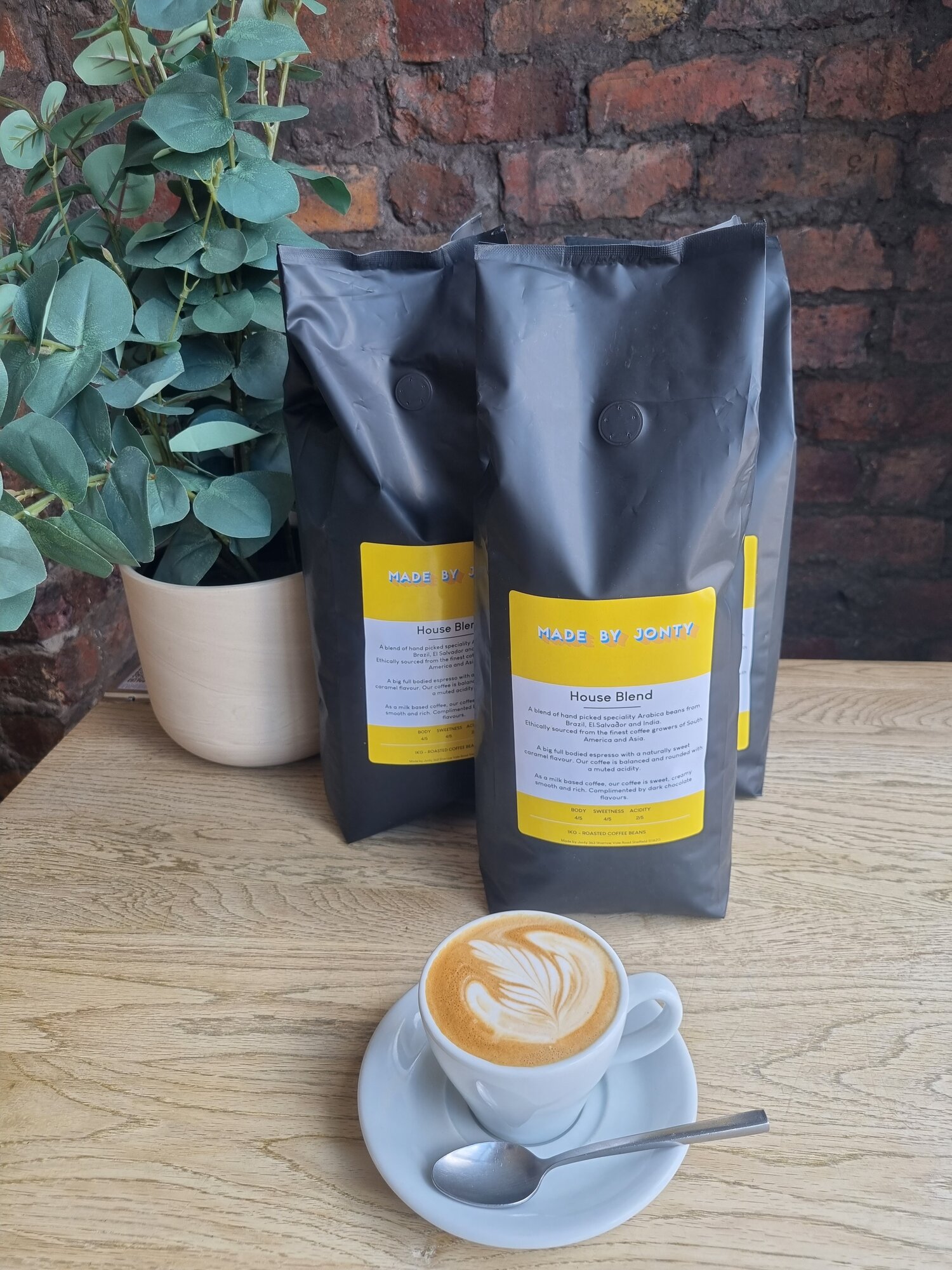 A cup of coffee on a table, along side some bags of coffee beans,  at Made by Jonty.