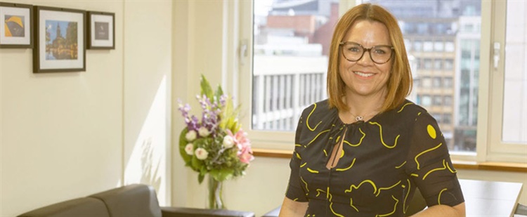A woman stands amiling atthe camera in an office.