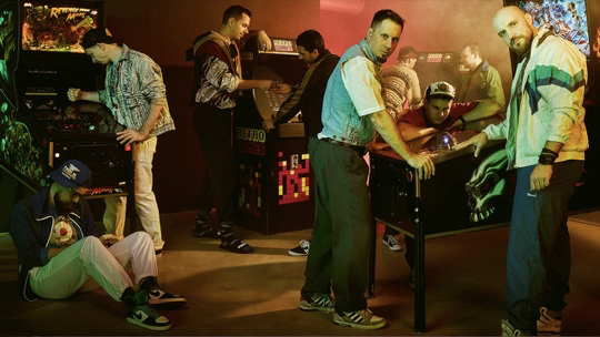 Sumo Digital - 9 men posing around arcade machines.