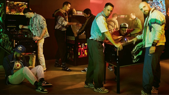 Sumo Digital - 9 men posing around arcade machines.