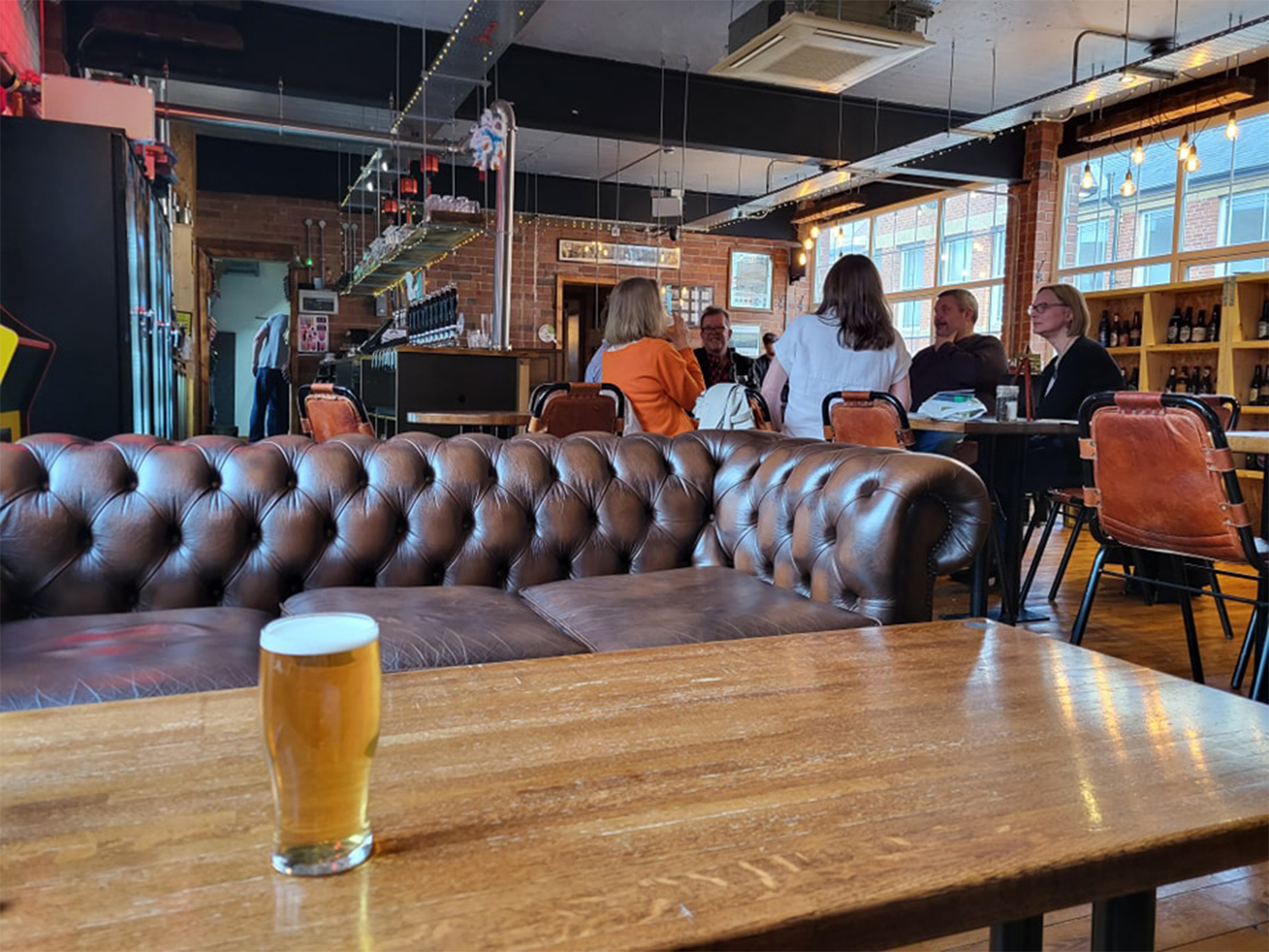 Inside at Perch Brewhouse, a pint of beer stands on a wooden table. Behind the table is a leather sofa.