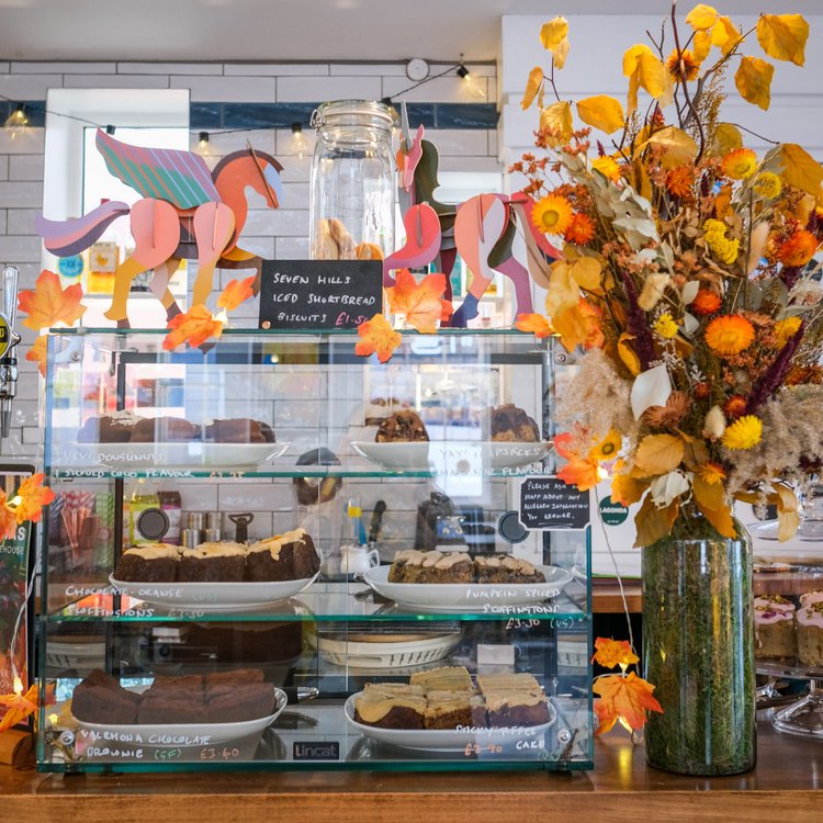A glass display case sits on a counter, at The Treehouse Cafe, filled with cakes and pastries.