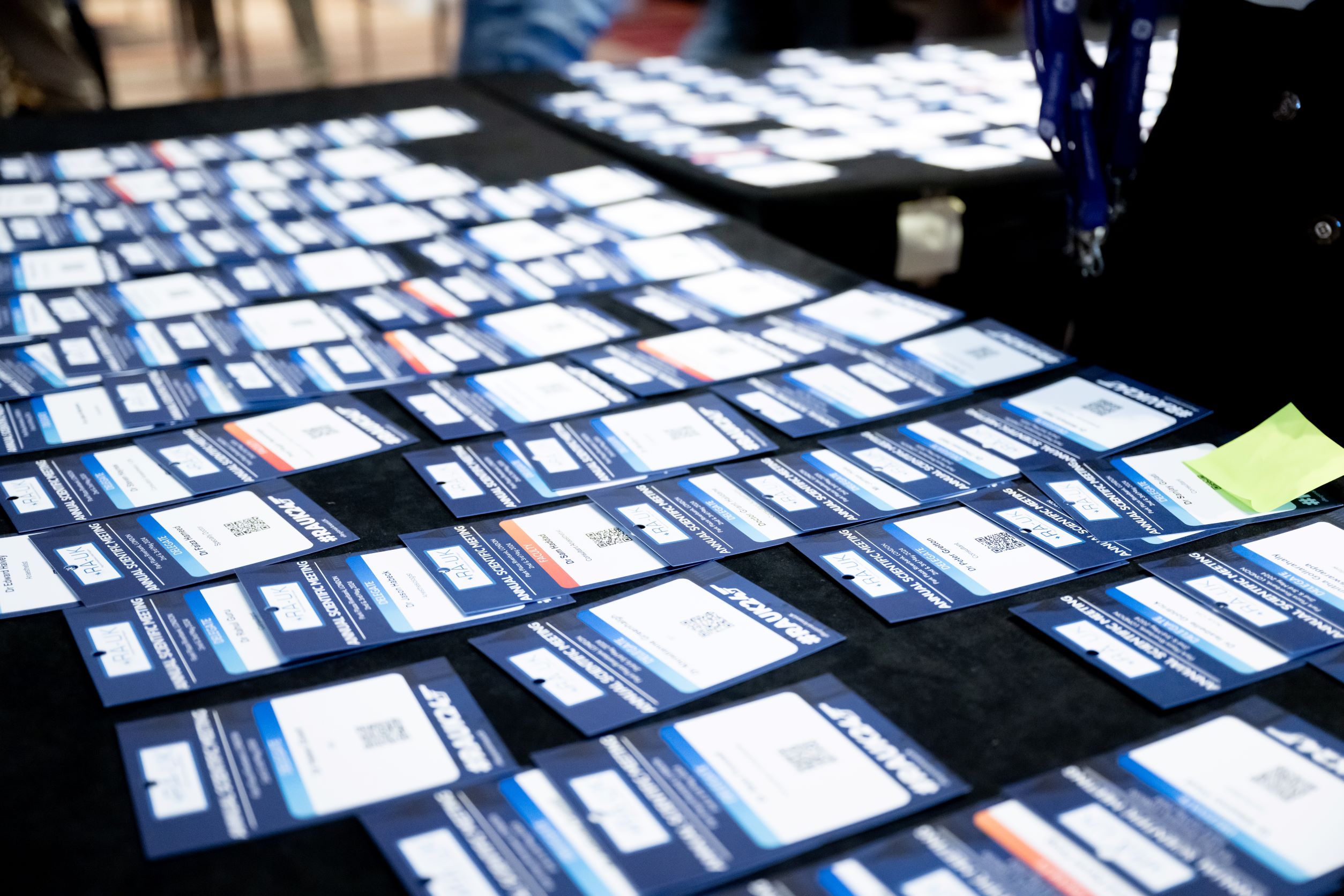 Table covered with numerous blue and white delegate badges arranged in rows, each featuring a name, QR code, and event branding.