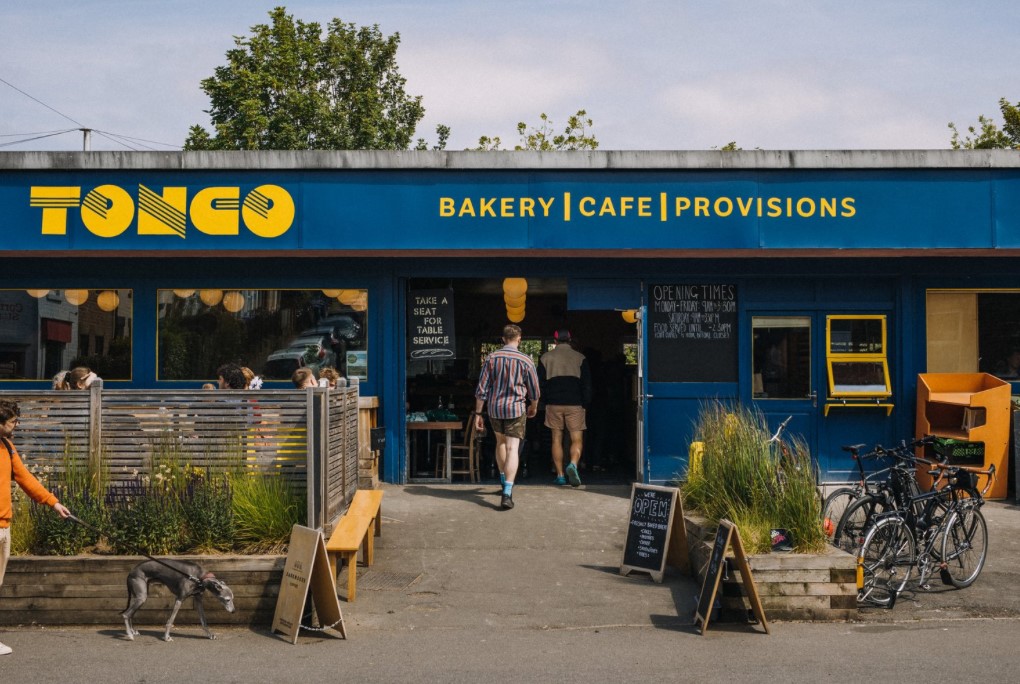 The exterior of a building painted blue. There is yellow lettering above the window and door that reads ' Tonco' and 'Bakery, Cafe, Provisions'.